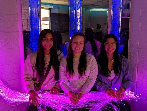 Three students sit in the Utica University Sensory Room, with purplish-blue lights on.